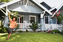 Boy with toy airplane in front yard of house