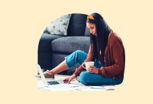 A woman, looking at her laptop and holding a cup of coffee