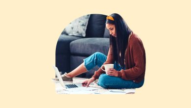 A woman, looking at her laptop and holding a cup of coffee